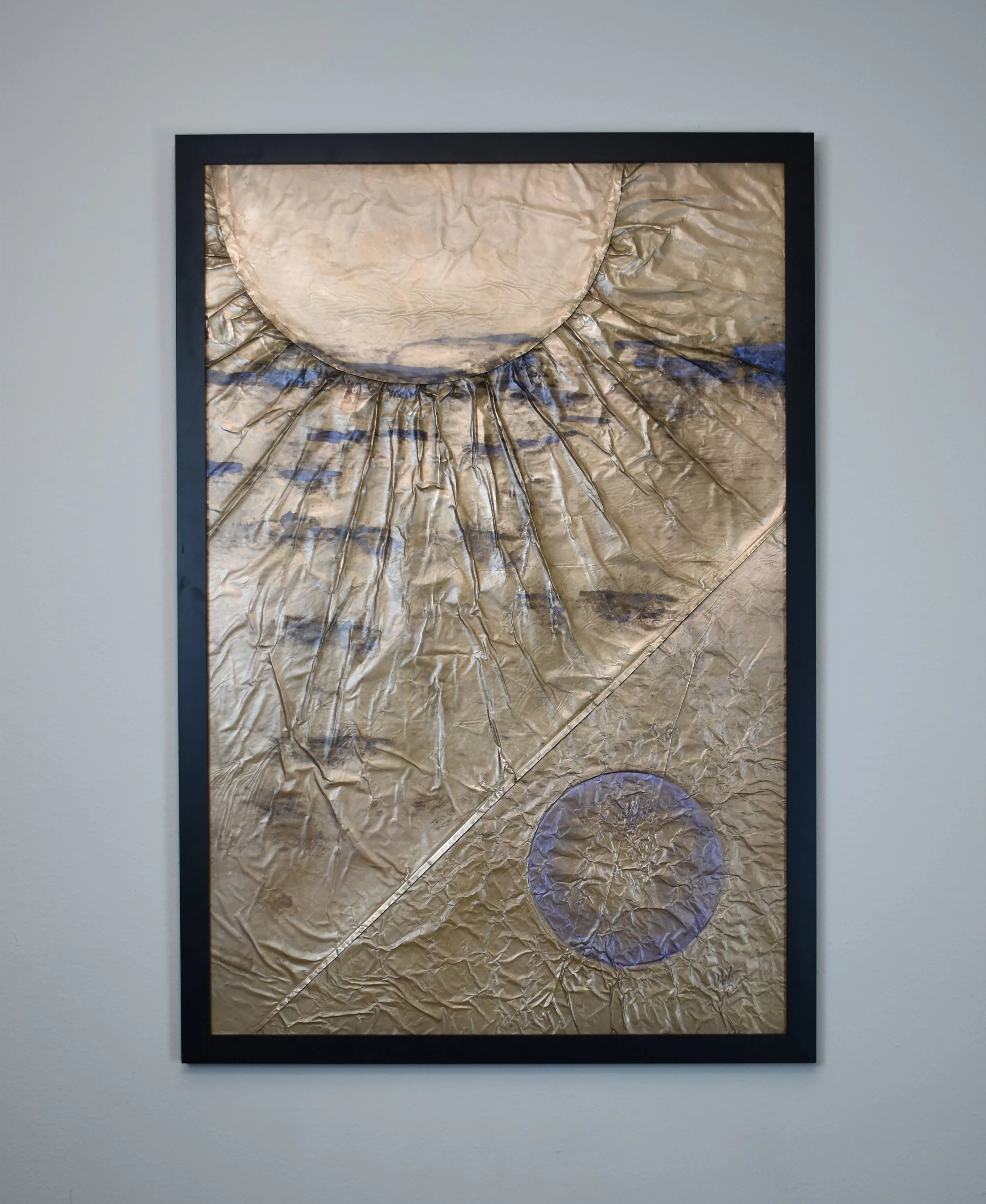 Textured gold-toned abstract artwork featuring a large circular form above, a smaller violet circle below, and radiating geometric lines. Displayed on a white wall.