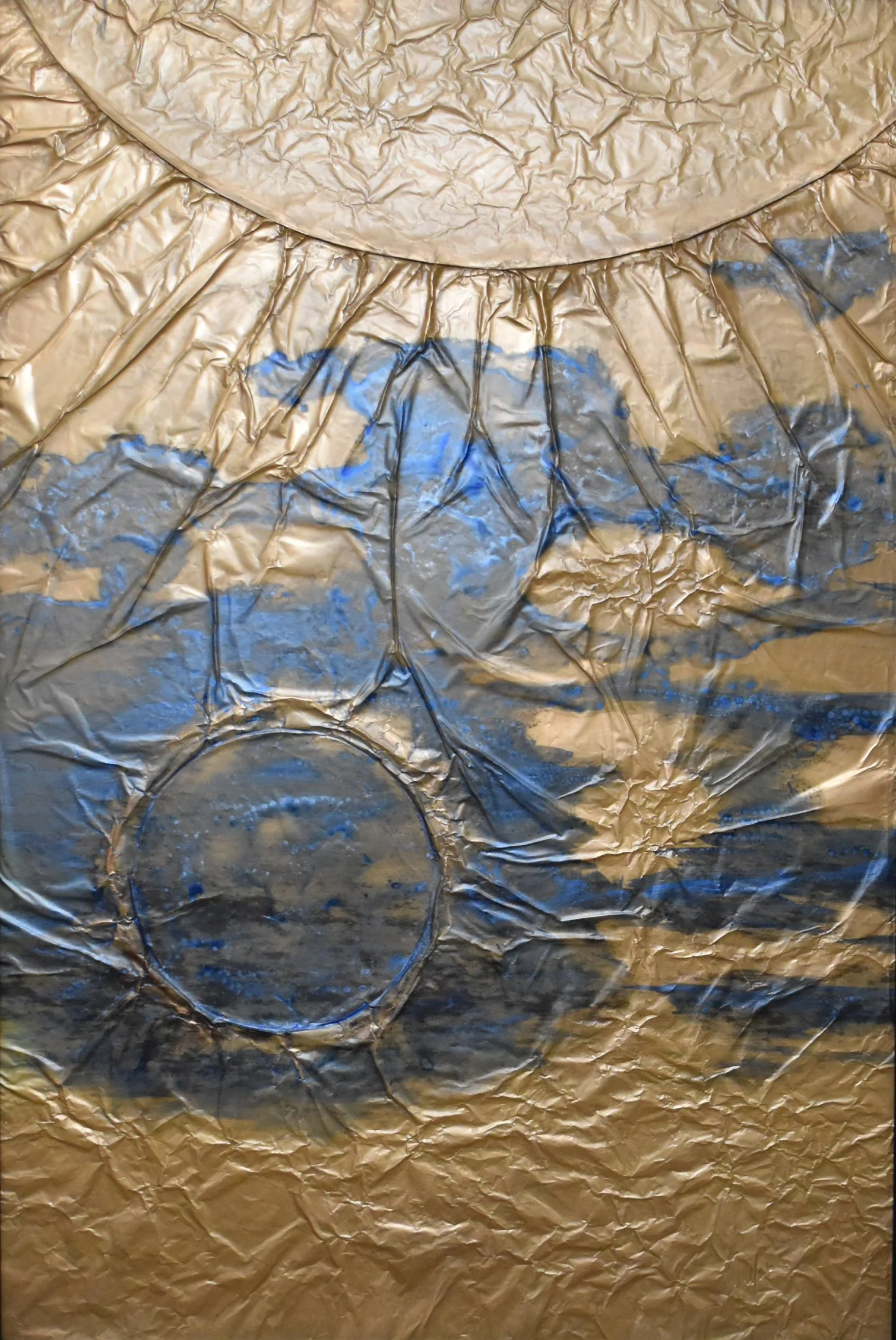 Textured gold-toned abstract artwork with blue and black markings, featuring a large curved form above and a dark circular form below. Shown close up without a frame.