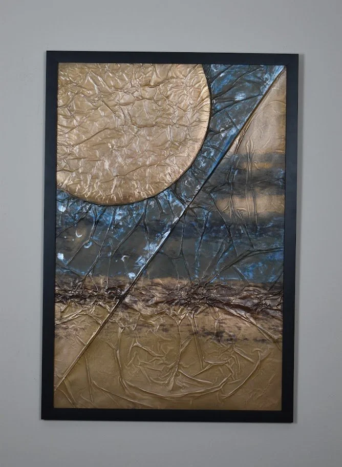 A golden orb intersects sweeping blue and metallic planes. Displayed framed on a white wall.
