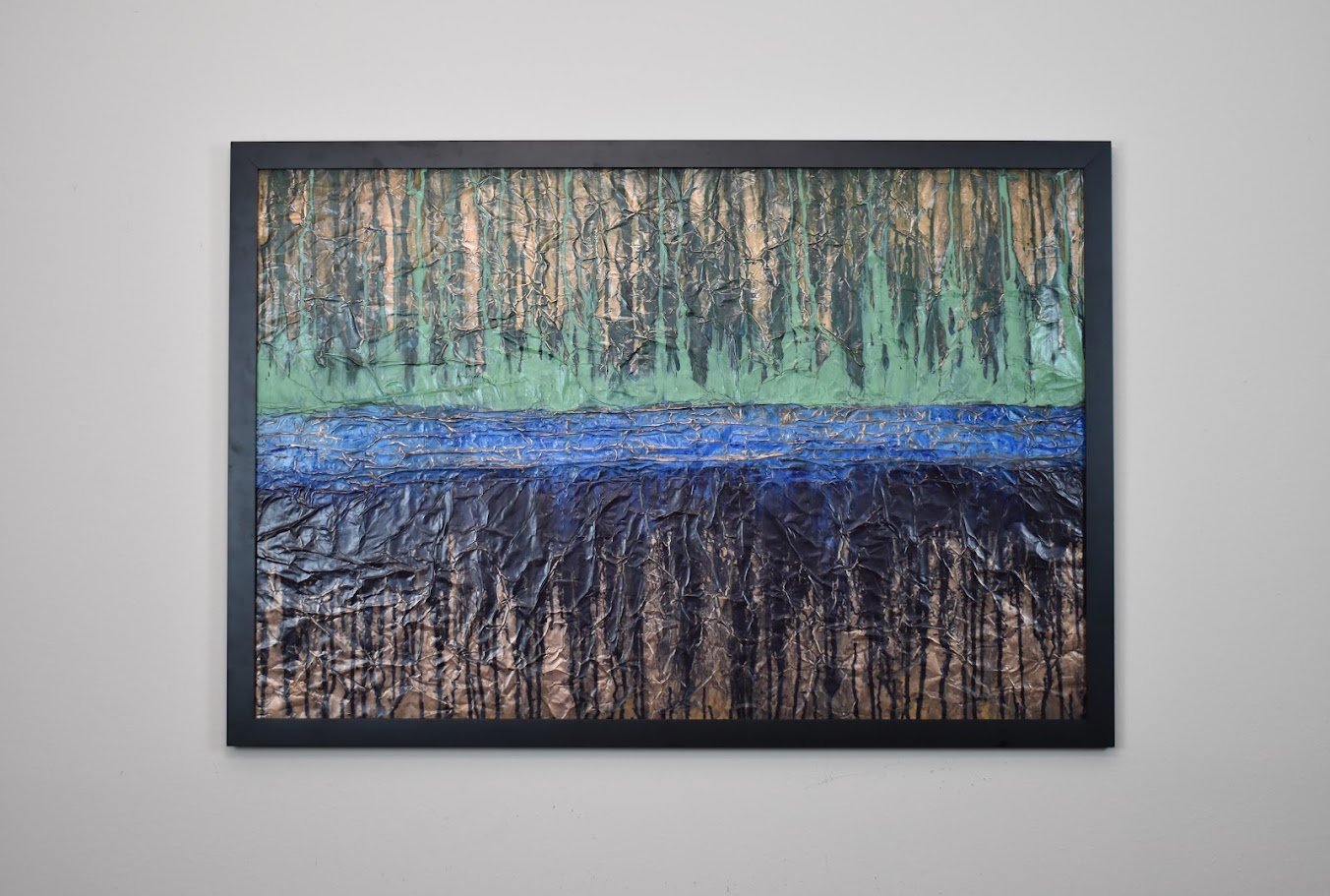Layered bands of green, blue, and black evoke a distant abstract landscape. Displayed framed on a white wall.