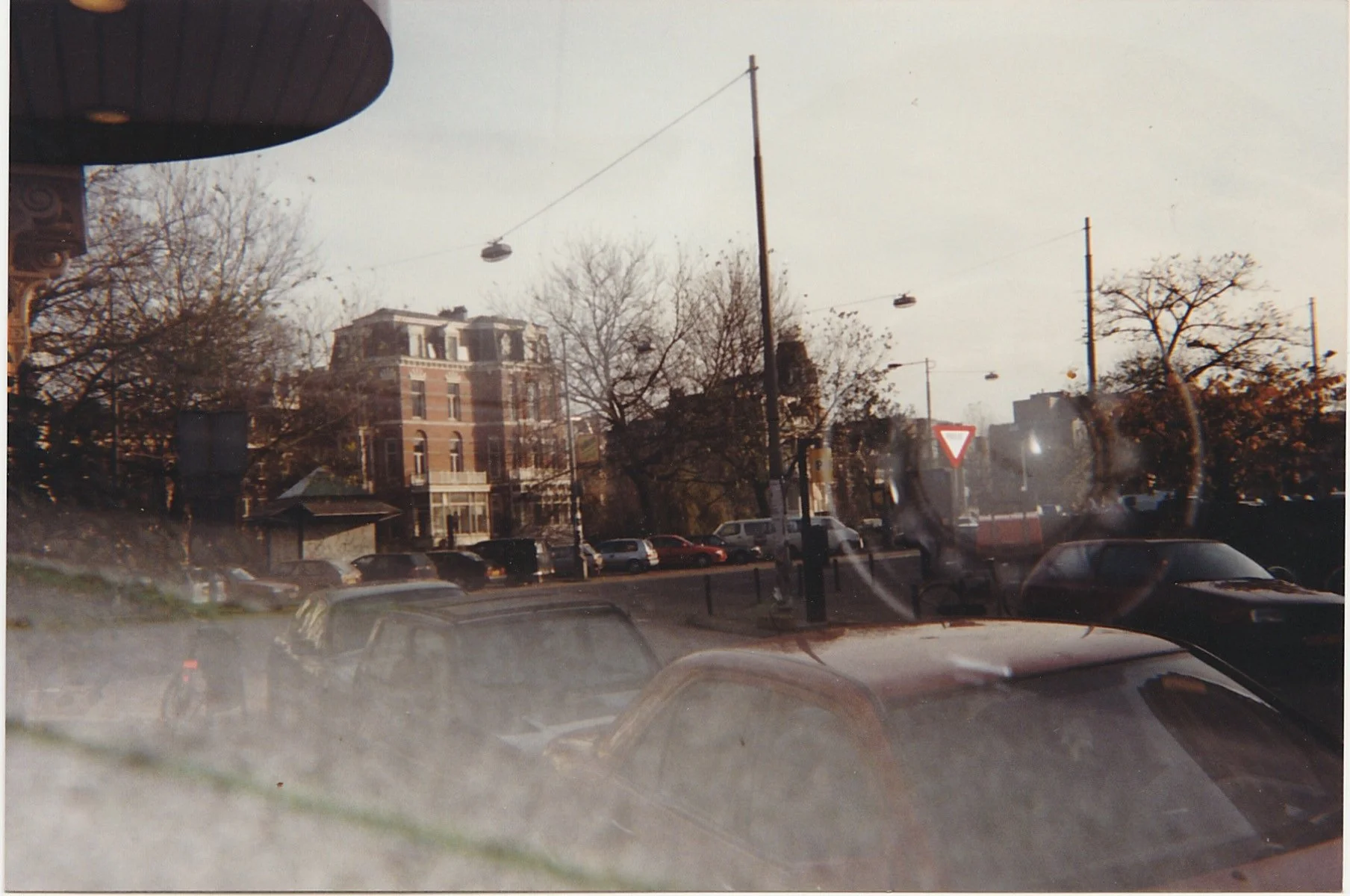 Rainy city street viewed through a window, with cars and pedestrians blurred by moisture on the glass.