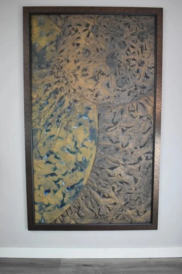 A golden planetary arc emerges from a fractured gray field. Displayed framed on a white wall.