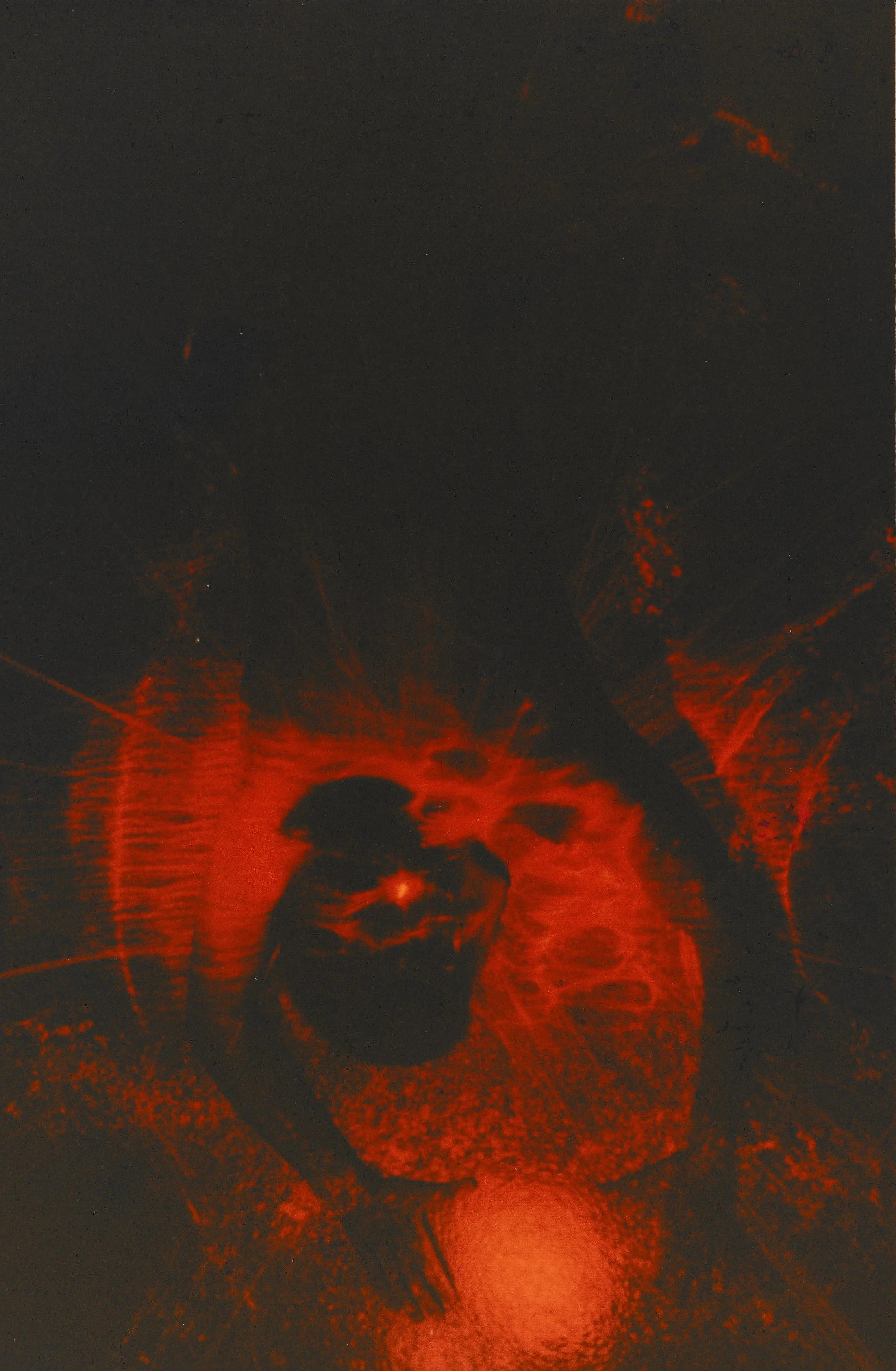 Bright red laser rays radiate outward from a sculptural form displayed on a pedestal in a dark room.