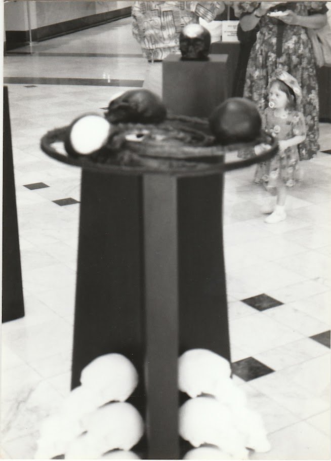 A central ring-like sculpture containing skull elements serves as the focal point of a gallery filled with skulls, exploring themes of time and transformation.