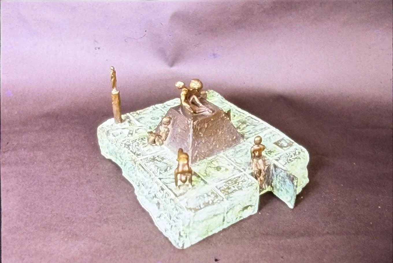 Patinated bronze platform sculpture centered on a stepped pyramid-like structure. Small human figures stand, climb, and gather around the elevated form.