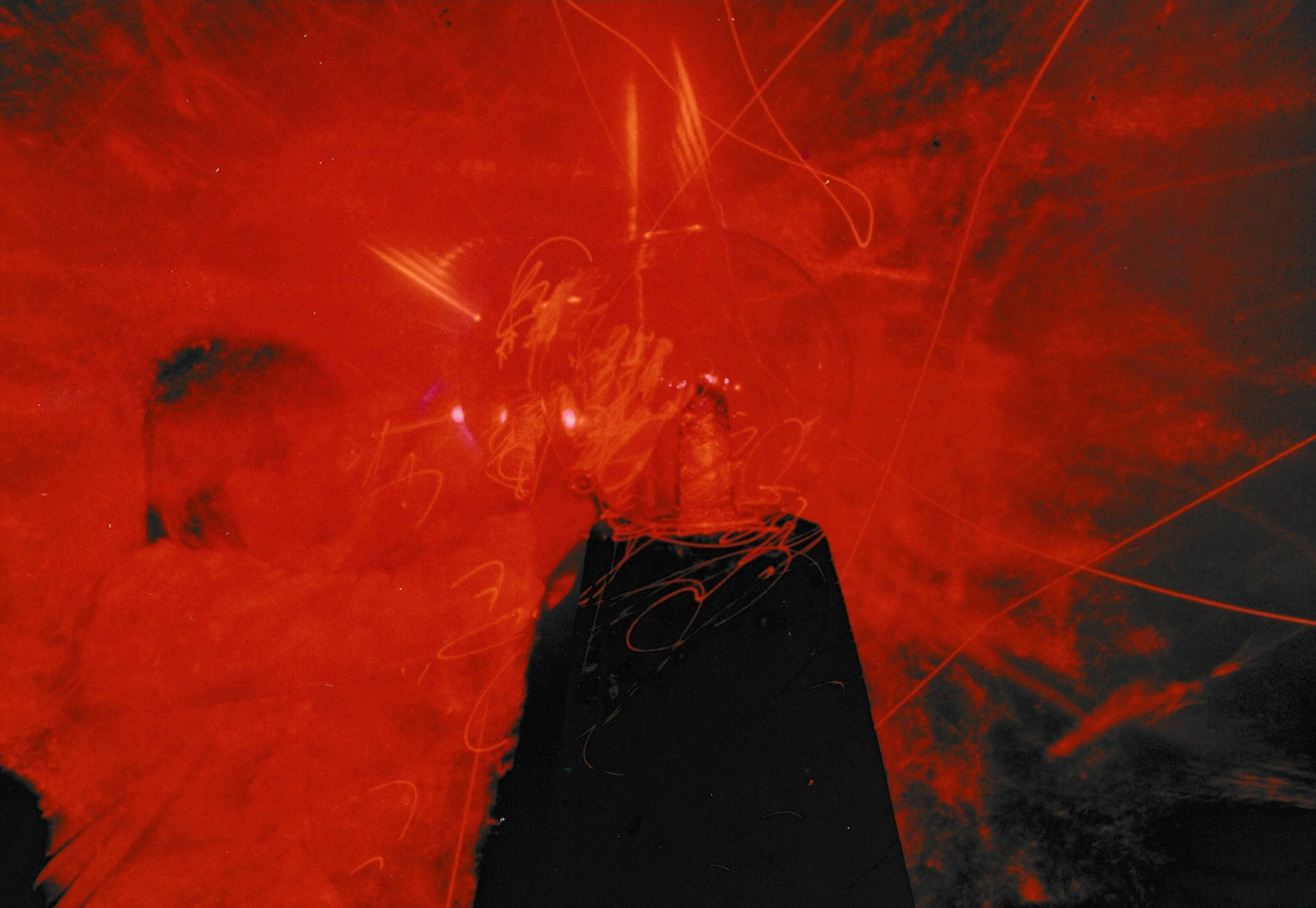 Dark gallery installation filled with sweeping red laser light trails radiating around sculptural forms and pedestals.