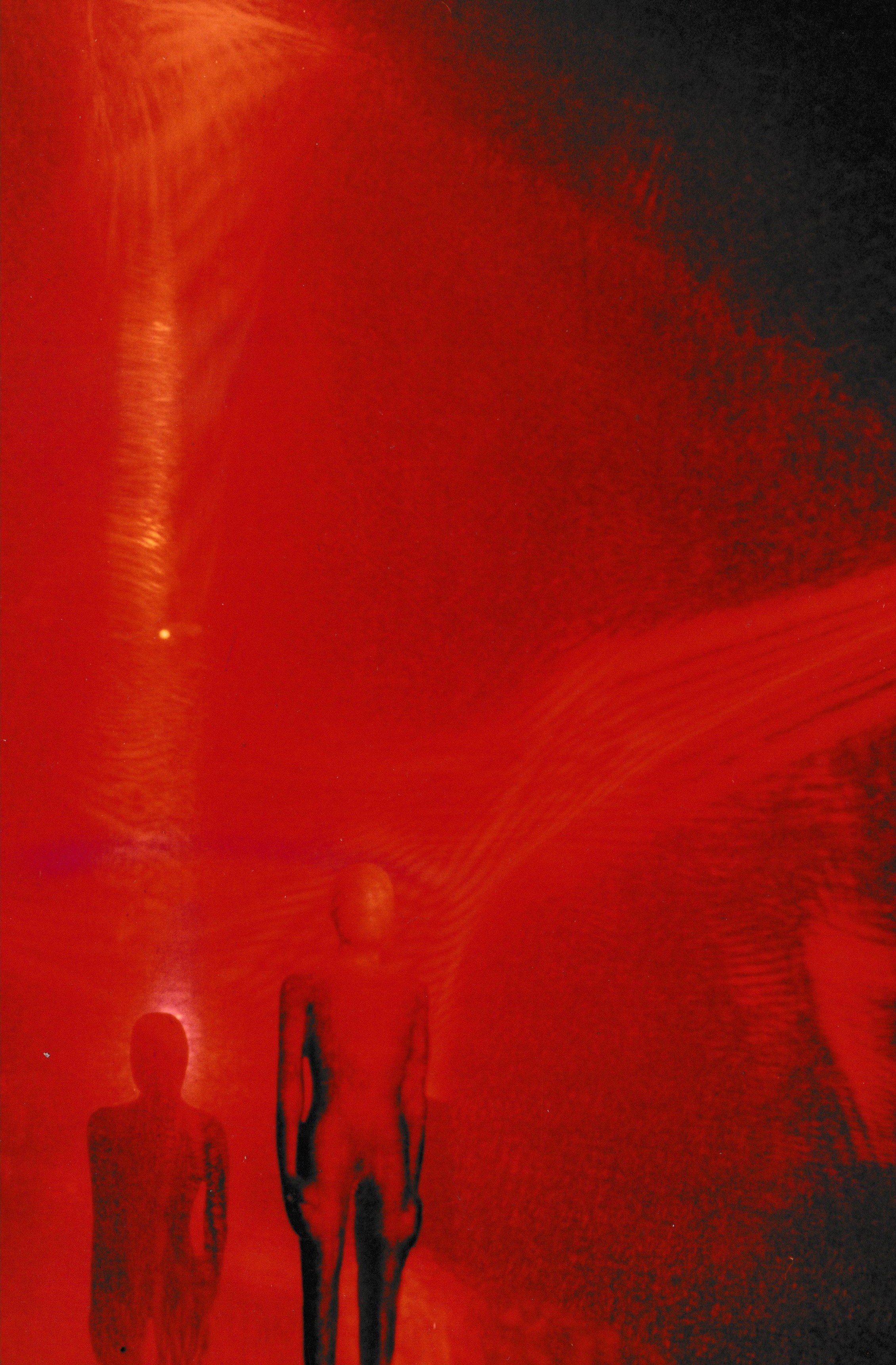 Red-lit scene featuring abstract sculptural forms partially obscured by glowing laser light and atmospheric haze.