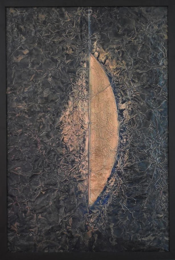 A golden crescent emerges from a dark, textured field. Shown close up in a black frame.