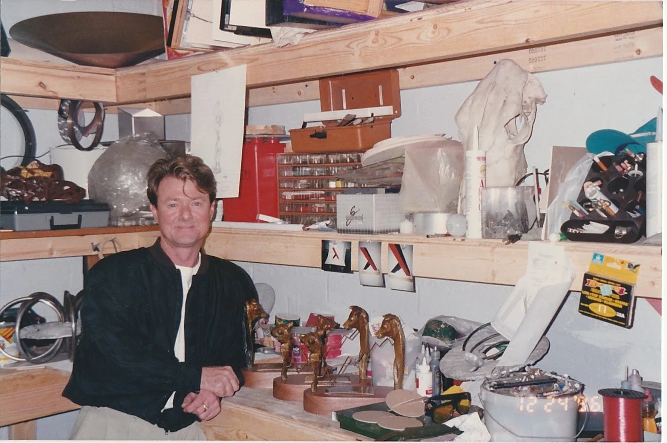 Whitney Wolf II leaning against a shelf in his warehouse surrounded by tools and art.