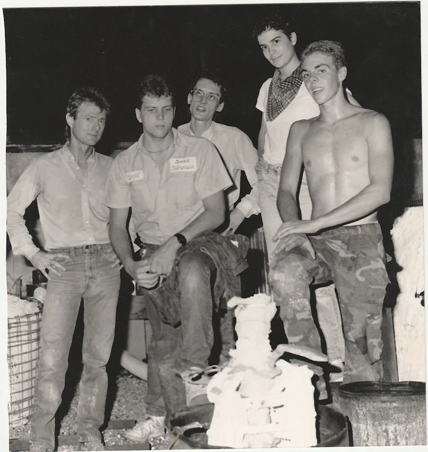 Black and white photo of a group of friends hanging out one night around bronze casting equipment. Whitney Wolf II is the first person on the right.