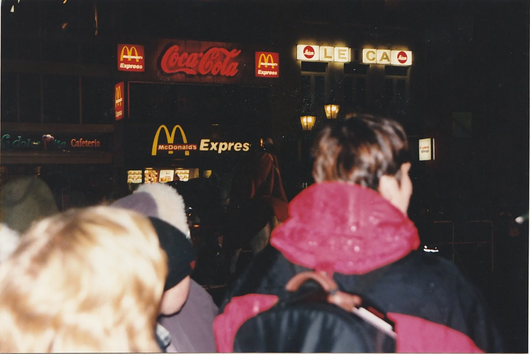 Crowd gathered beneath glowing restaurant and storefront signs after dark.