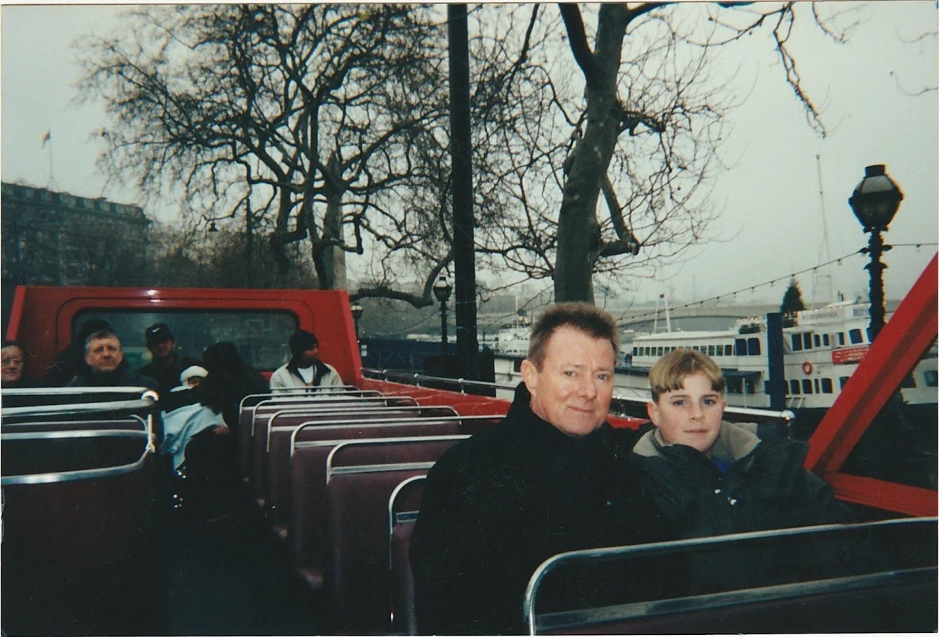 Whitney Wolf II and his son Whitney Wolf II sit on the top of a double decker bus on a gray European day. EST 1990s