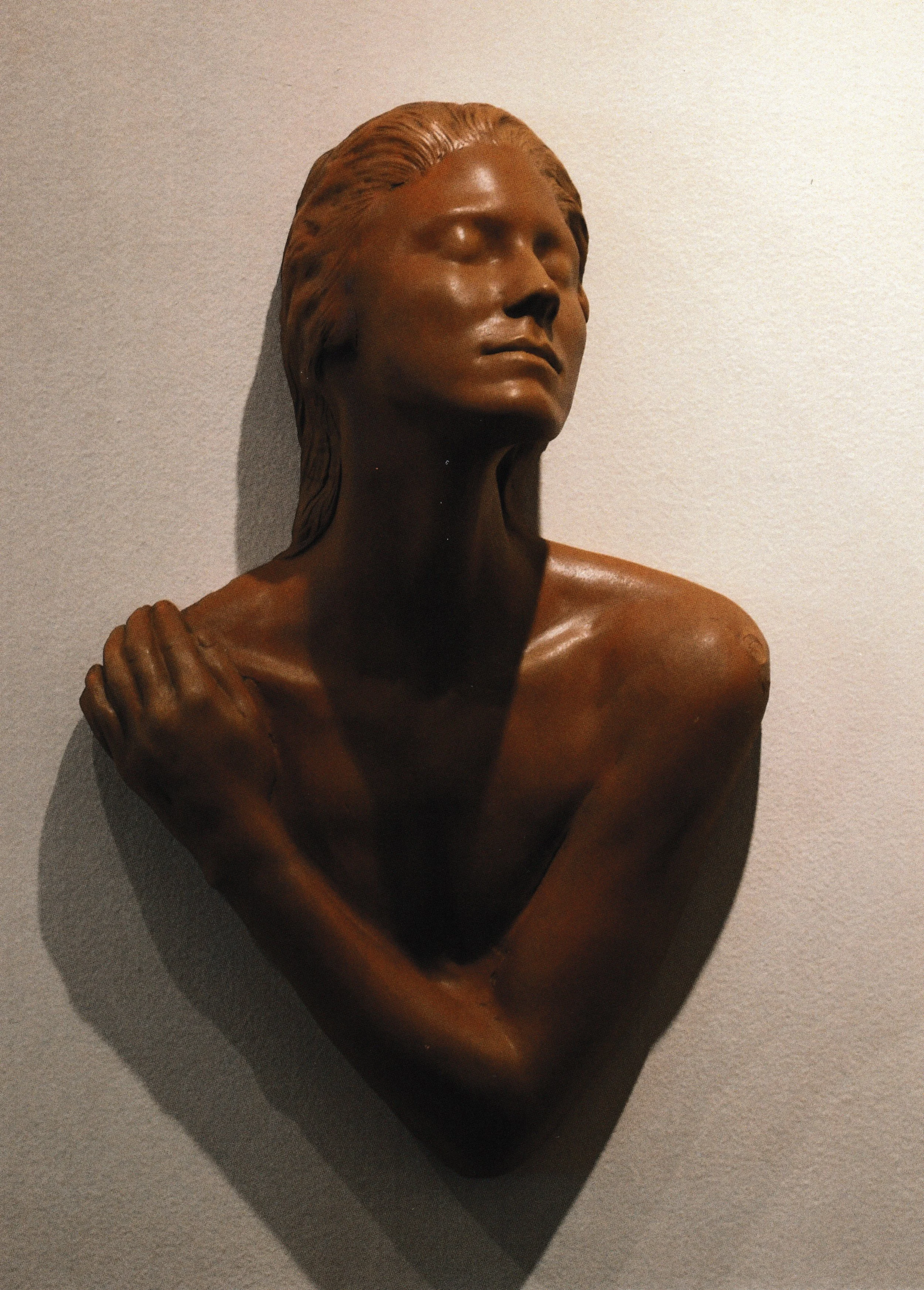 Terracotta life mask of a female bust with crossed arms and uplifted face, expressing quiet strength and contemplation.