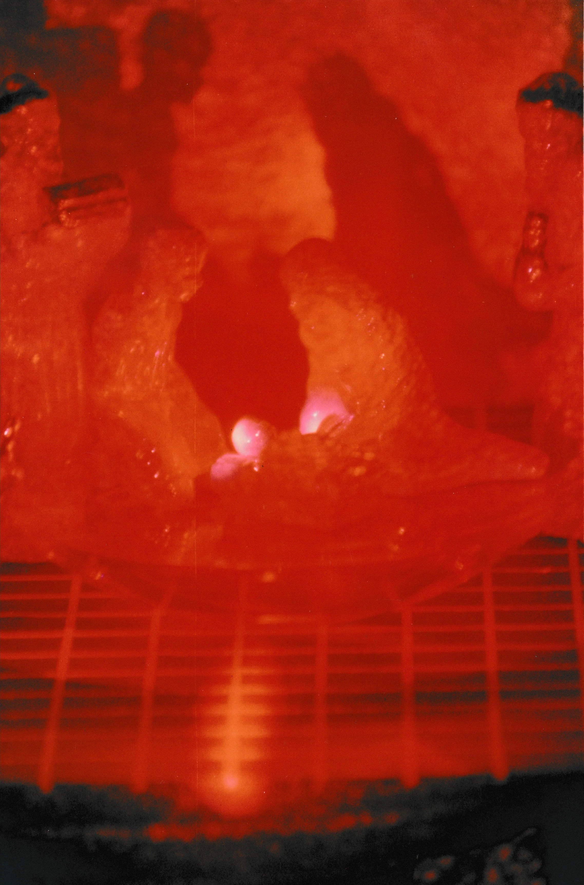Red laser installation featuring glowing sculptural forms and vertical structures emerging from a darkened space.