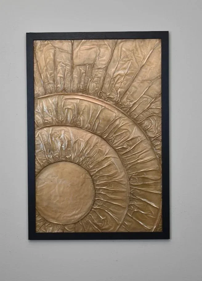 Concentric golden forms radiate outward like waves of energy. Displayed framed on a white wall.