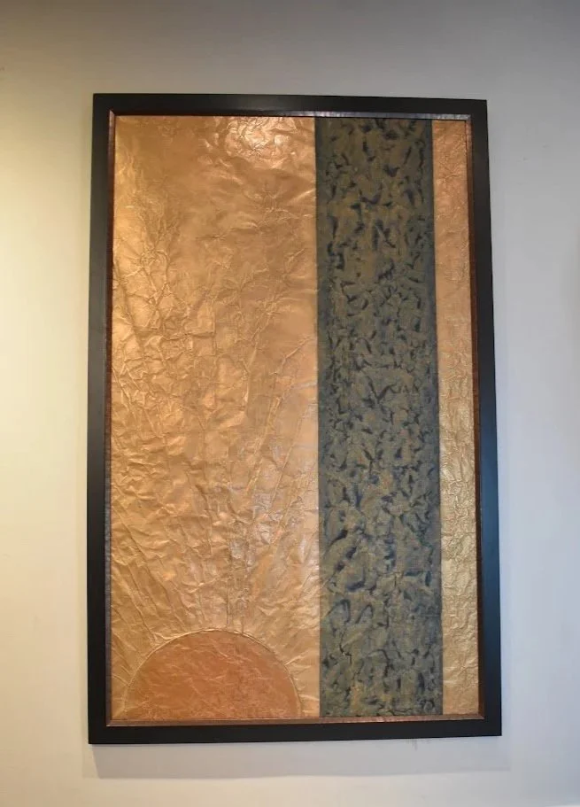 A golden orb rises beside a dark vertical band. Displayed framed on a white wall.
