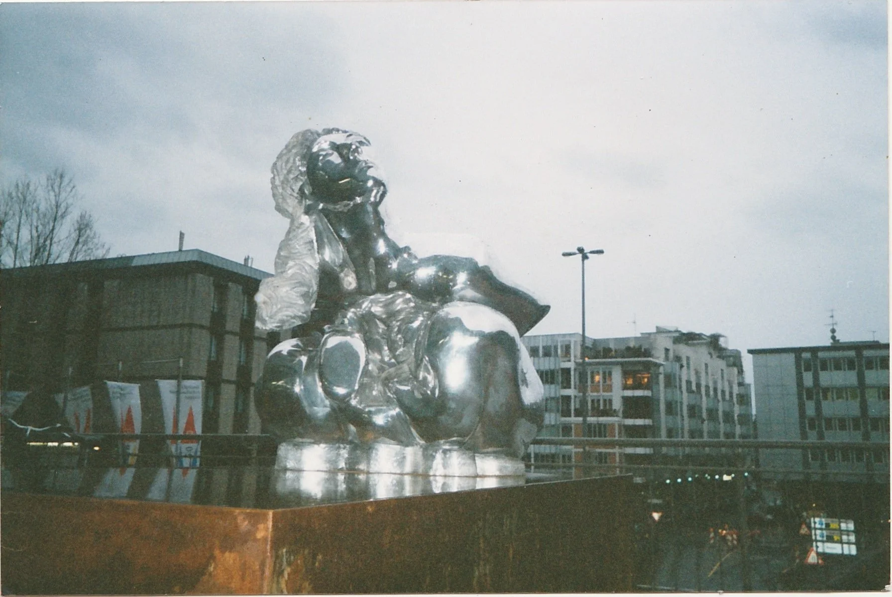 Reflective silver sculpture with flowing organic forms situated in an urban square.