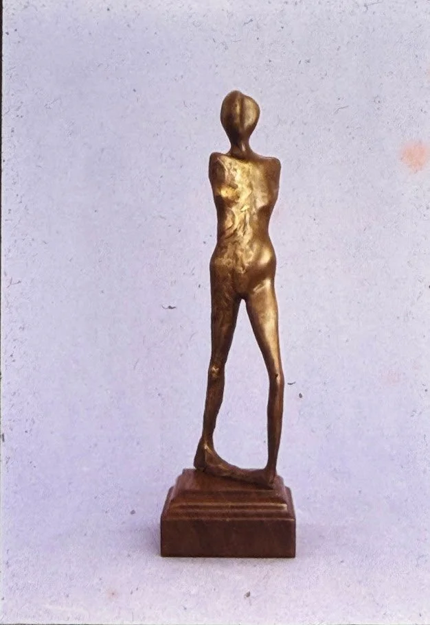 Tall bronze standing nude with narrow shoulders, long legs, and a subtly textured surface that emphasizes vertical movement.