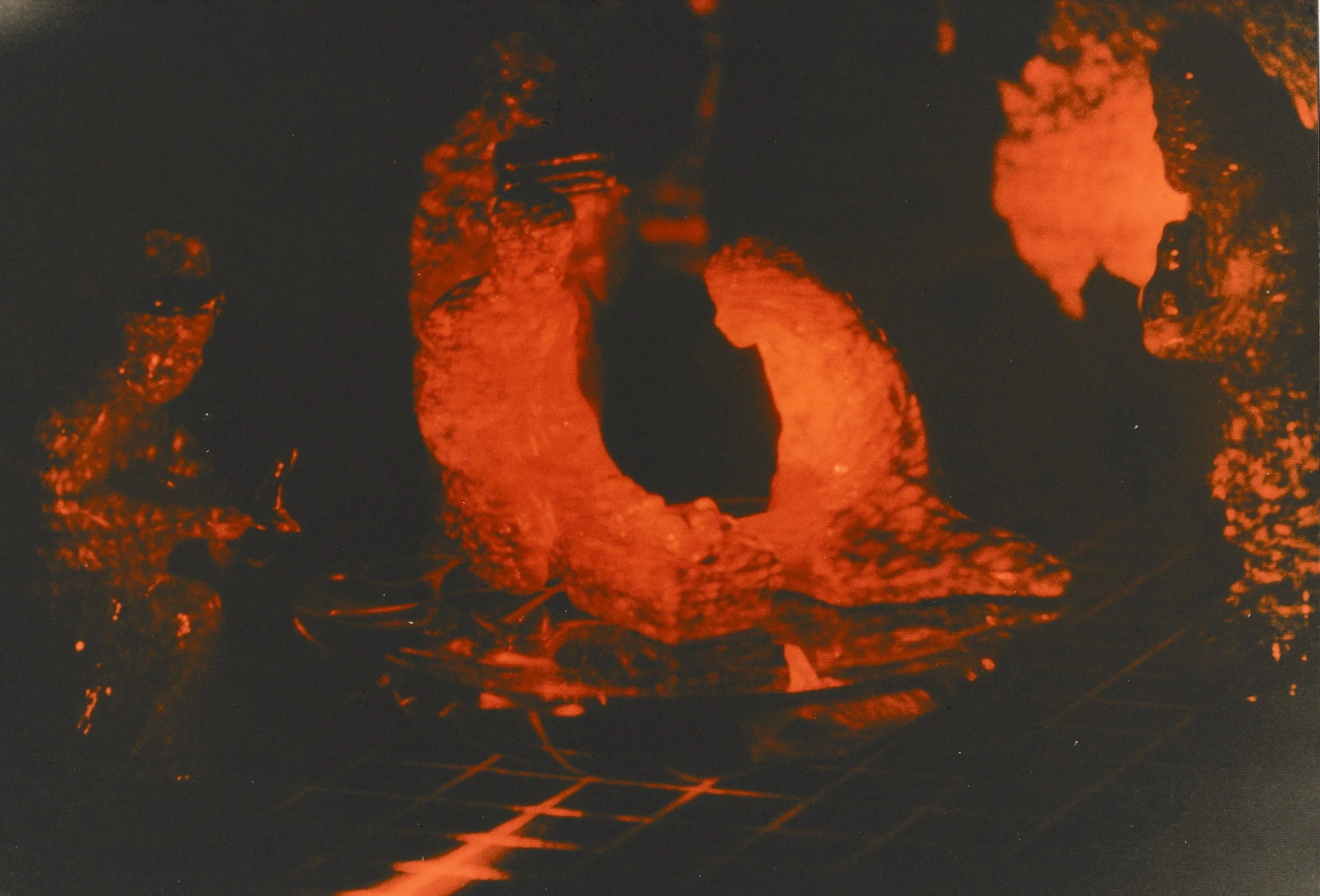 Abstract sculptural installation illuminated by red laser light, featuring rough organic forms surrounding a glowing ring-shaped structure positioned on a gridded surface.