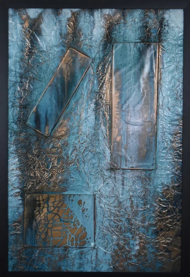 Geometric forms float within a textured field of luminous blue and metallic bronze. Shown close up in a black frame.