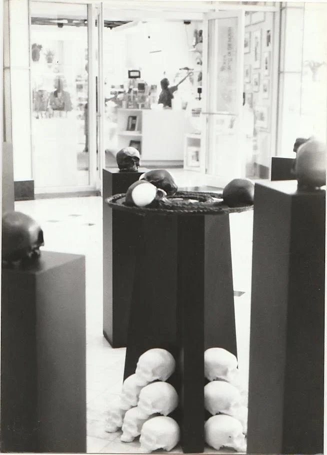 A central pedestal supports a circular sculptural arrangement surrounded by individual skull sculptures displayed on freestanding columns.