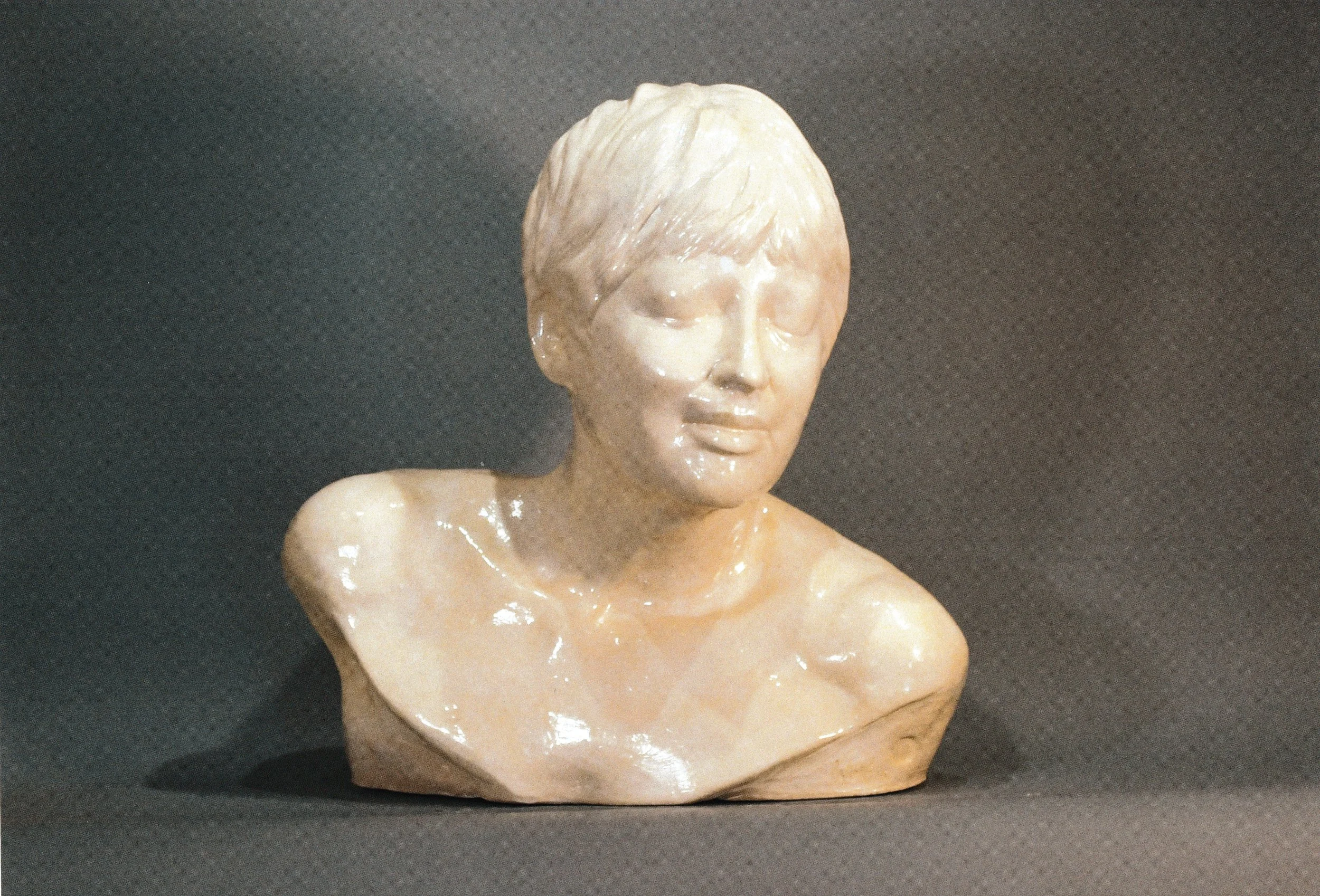 Ceramic life cast bust of a short-haired young person with closed eyes and a subtle, peaceful smile.