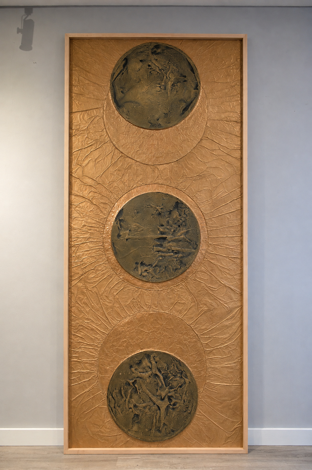 Three dark orbs align within a radiant golden field. Displayed framed on a white wall.