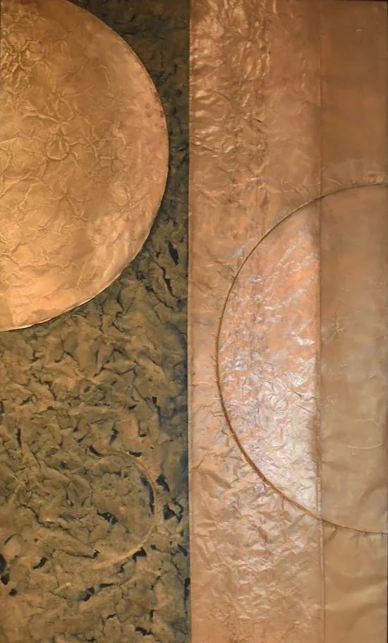 Two large circular forms enter from opposite sides of a divided metallic field. Displayed framed on a white wall.  Shown close up without a frame.