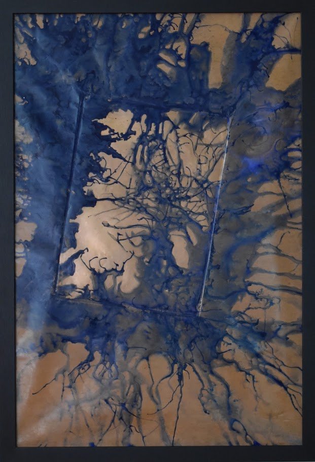 Deep blue currents spread across a warm metallic field. Shown close up in a black frame.