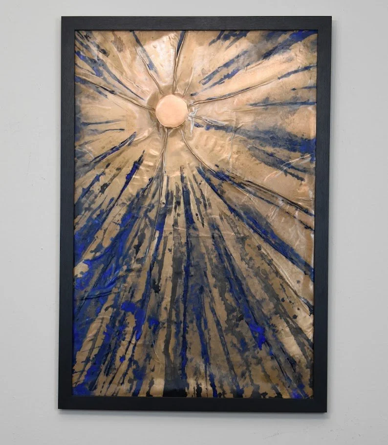 Radiating blue and gold lines burst outward from a luminous center. Displayed framed on a white wall.
