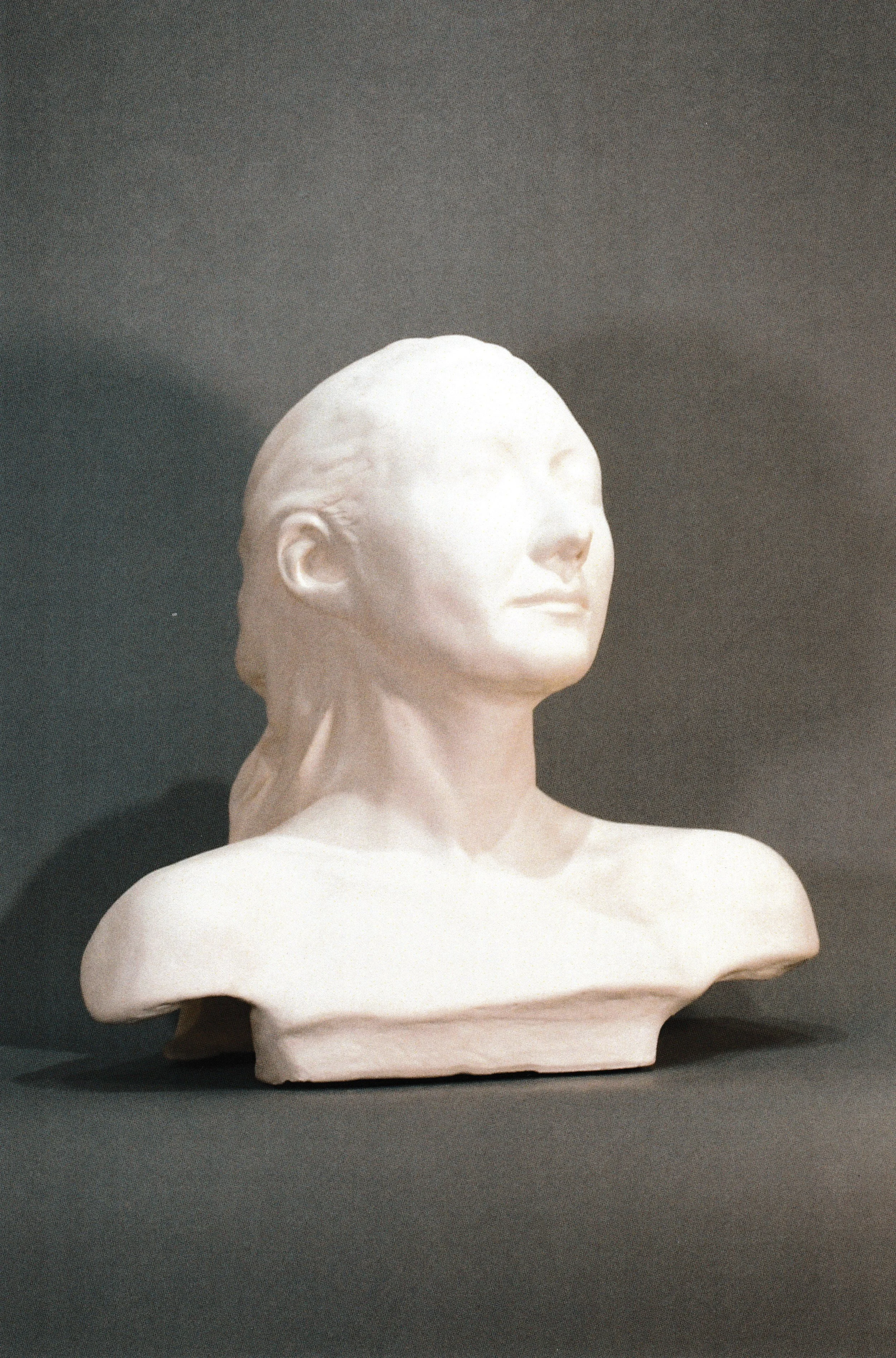 Ceramic life mask portrait with simplified features and tightly pulled-back hair, emphasizing the smooth geometry of the face.