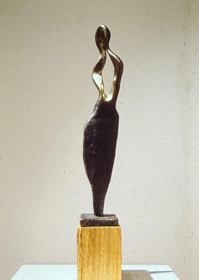 Abstract bronze female figure reduced to flowing curves and openings, standing on a circular wooden base.