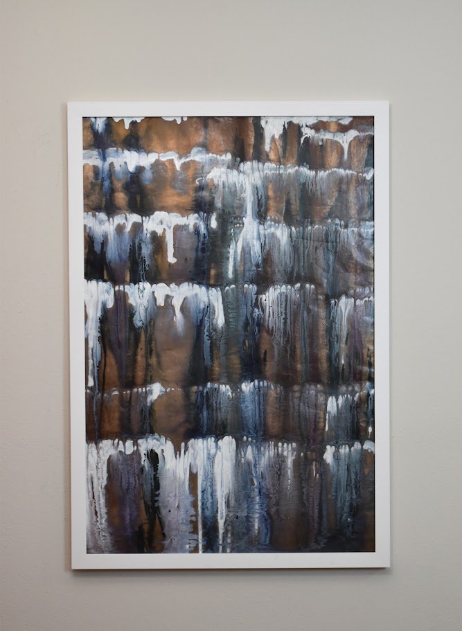 Layered white, blue, and bronze currents cascade across the surface. Displayed framed on a white wall.