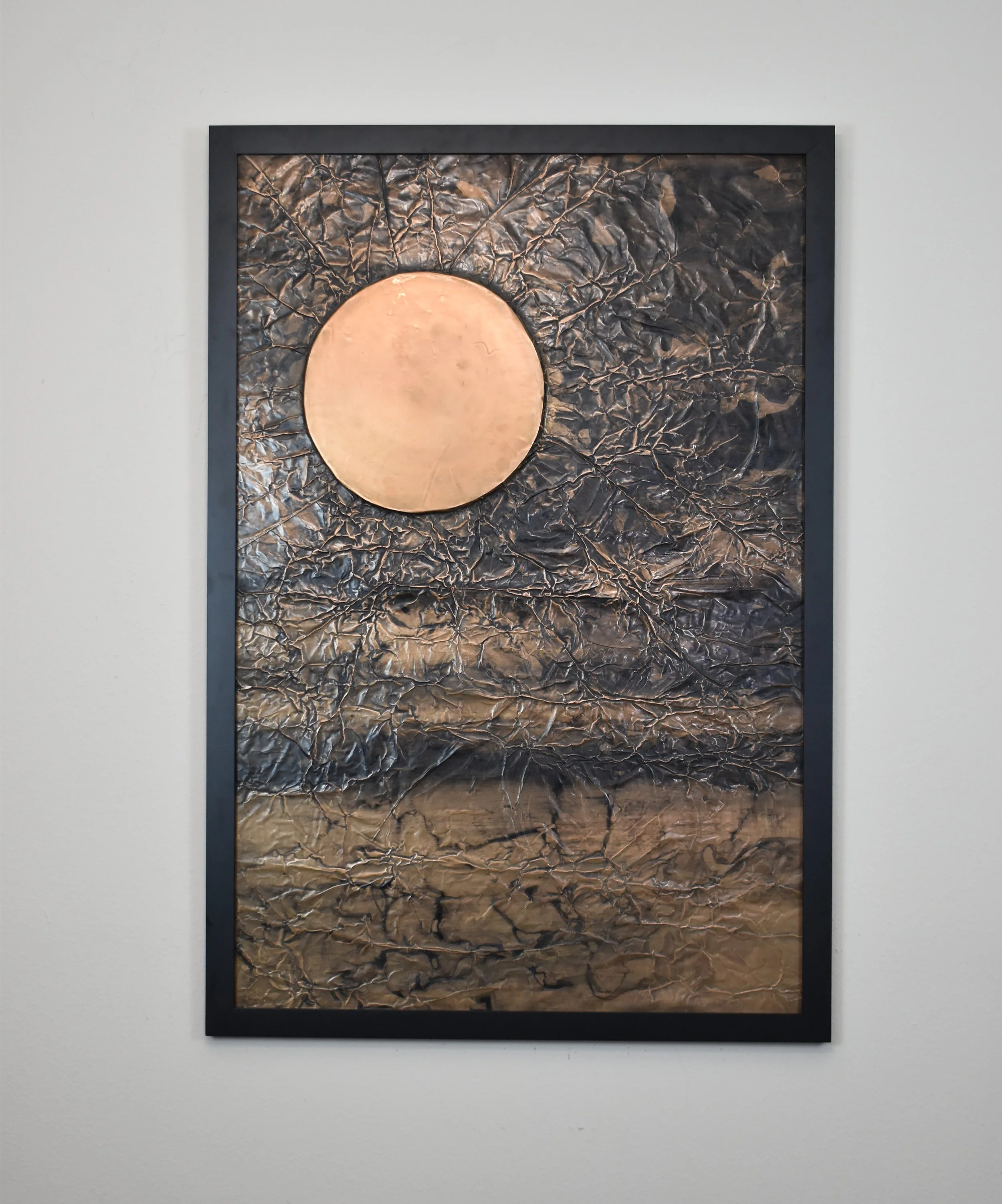 A golden orb floats within a dark, fractured metallic field. Displayed framed on a white wall.