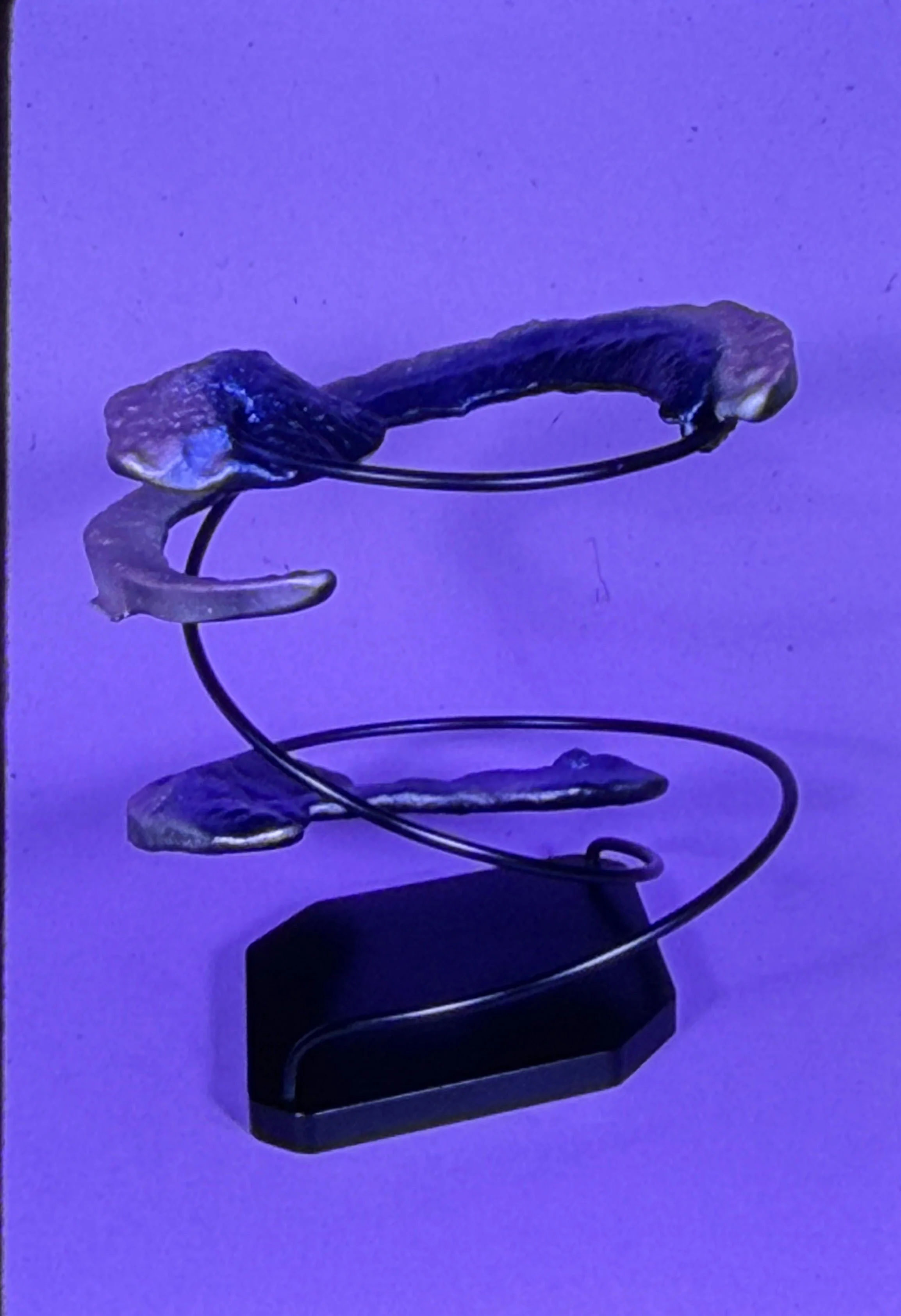 Compact sculpture featuring a textured horizontal form suspended within looping metal rings.