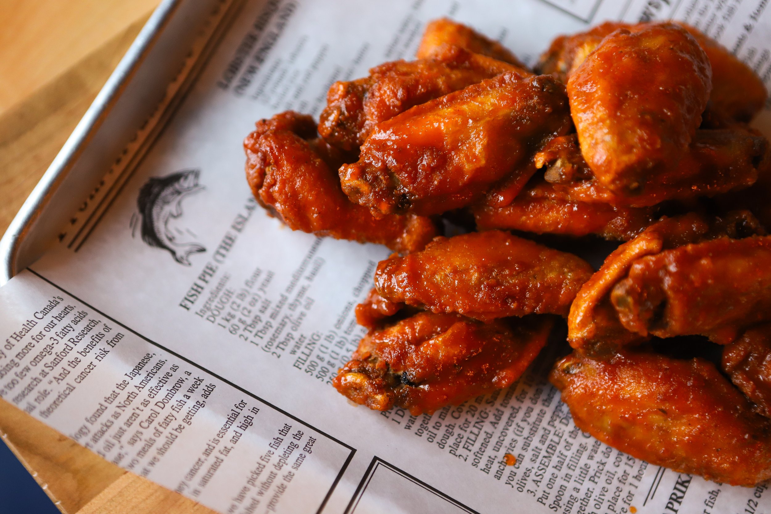 Close-up of chicken wings with your favourite sauce, placed on newspaper-lined tray.