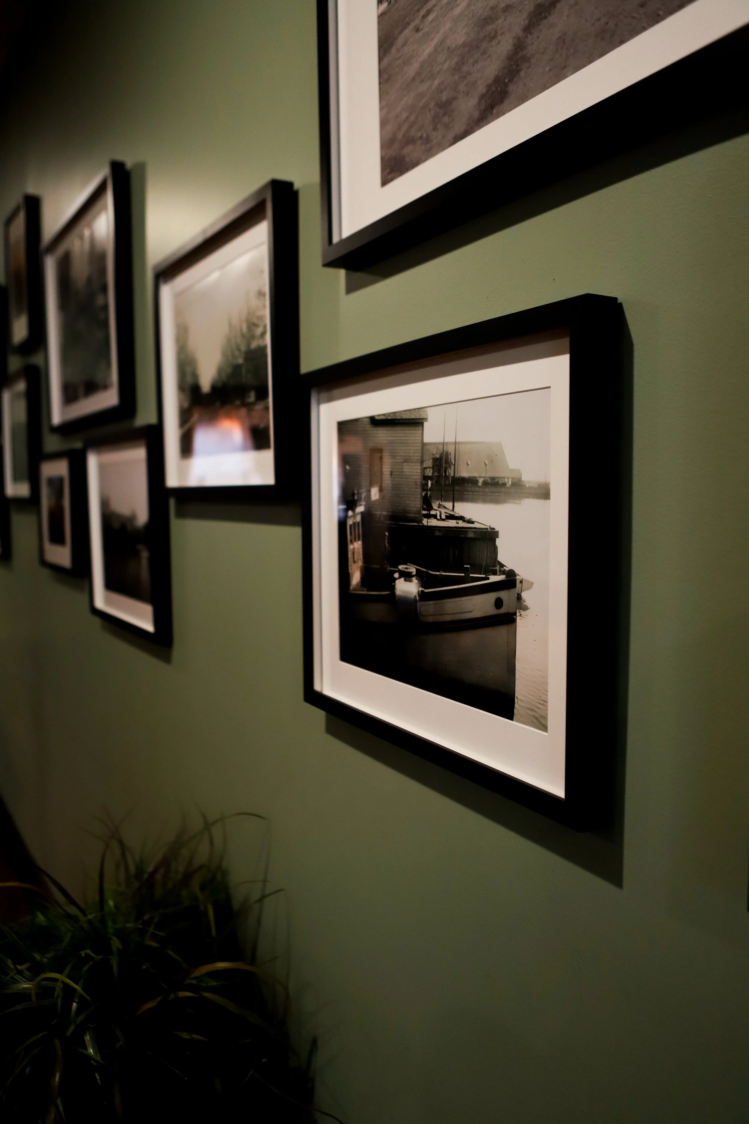 The Mackenzie Room closeup of a wall with multiple framed black and white photographs of Kincardine in the past, with some images showing boats and waterfront scenes, hung on a green wall.