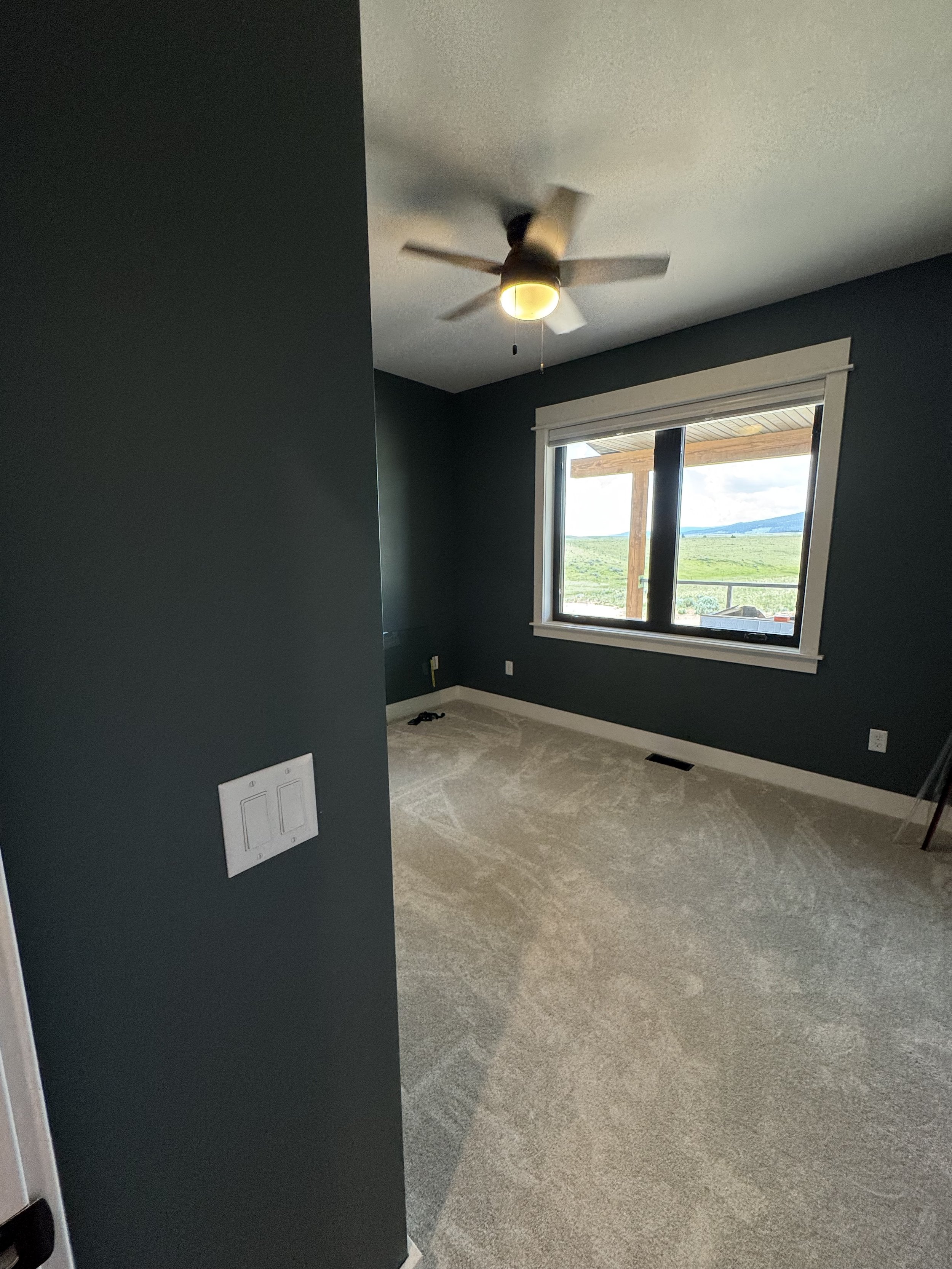 Custom bedroom with dramatic dark accent wall and designer ceiling fan — luxury Montana home by Mihelich Custom Builders near Butte.