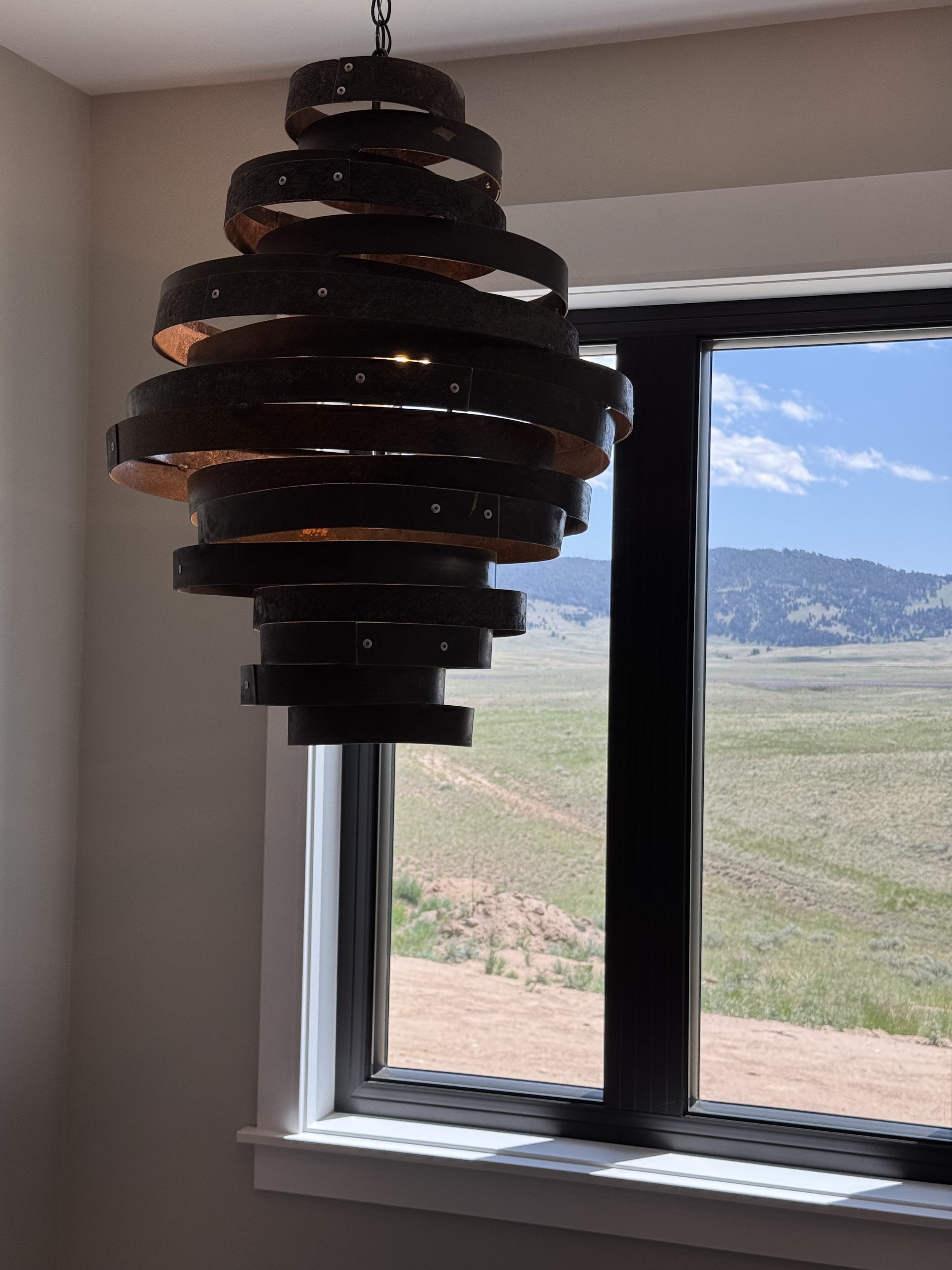 Dramatic statement pendant light with floor-to-ceiling windows and Montana mountain views — luxury custom home by Mihelich Custom Builders near Butte.