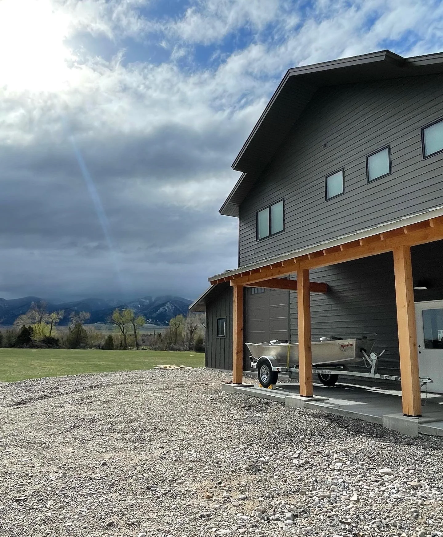 Black metal siding, timber accents, and mountain backdrop — River Barndominium custom build by Mihelich Custom Builders, Silver Star, Montana.