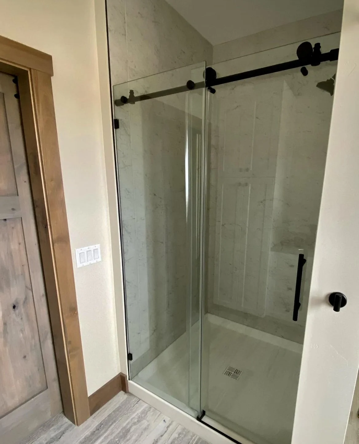 Custom bathroom with floor-to-ceiling tile and sliding barn door glass shower enclosure — luxury barndominium build in Silver Star, MT by Mihelich Custom Builders.