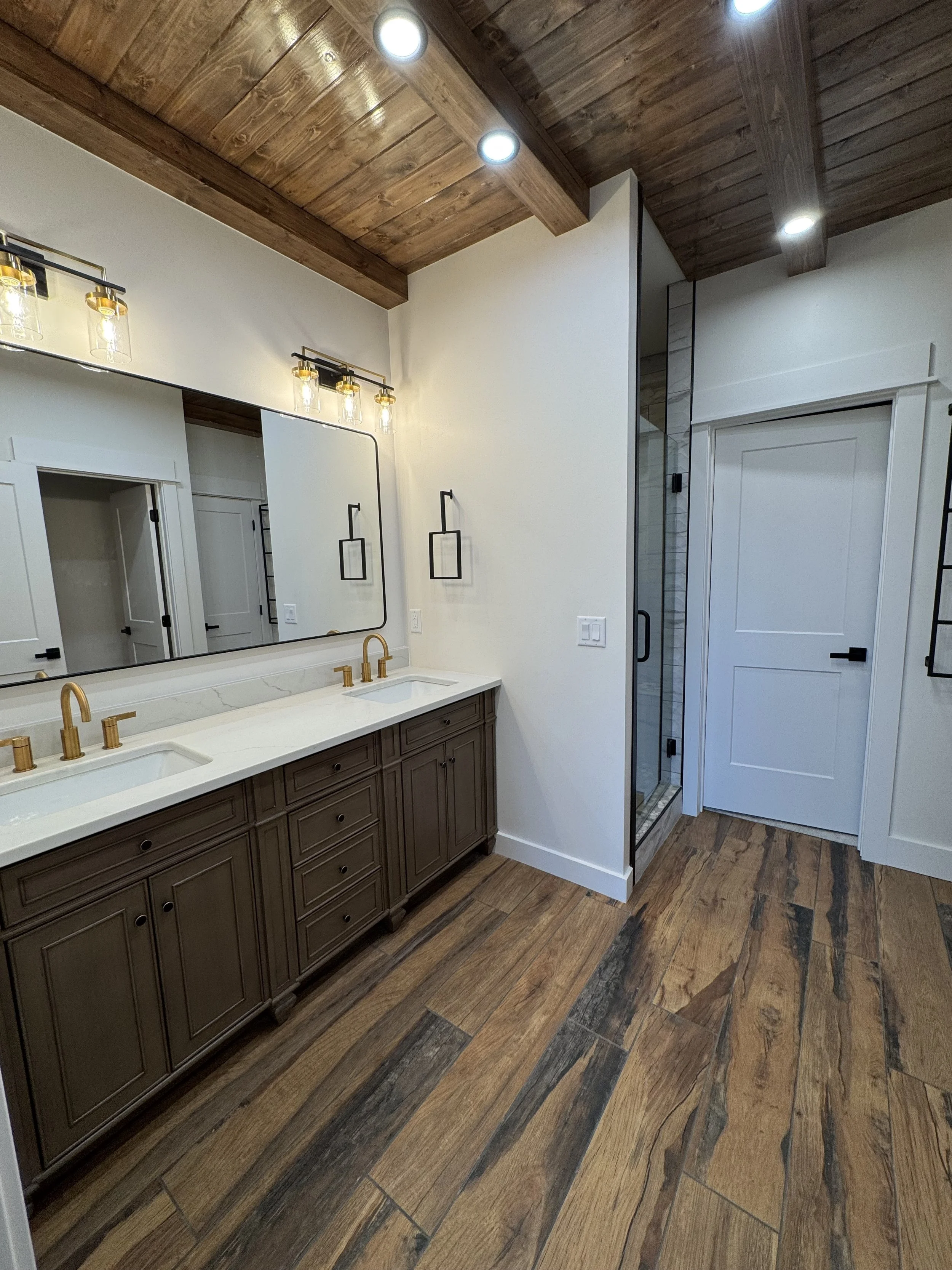 Custom double vanity with dark cabinetry and designer lighting — luxury primary bathroom by Mihelich Custom Builders near Butte, MT.