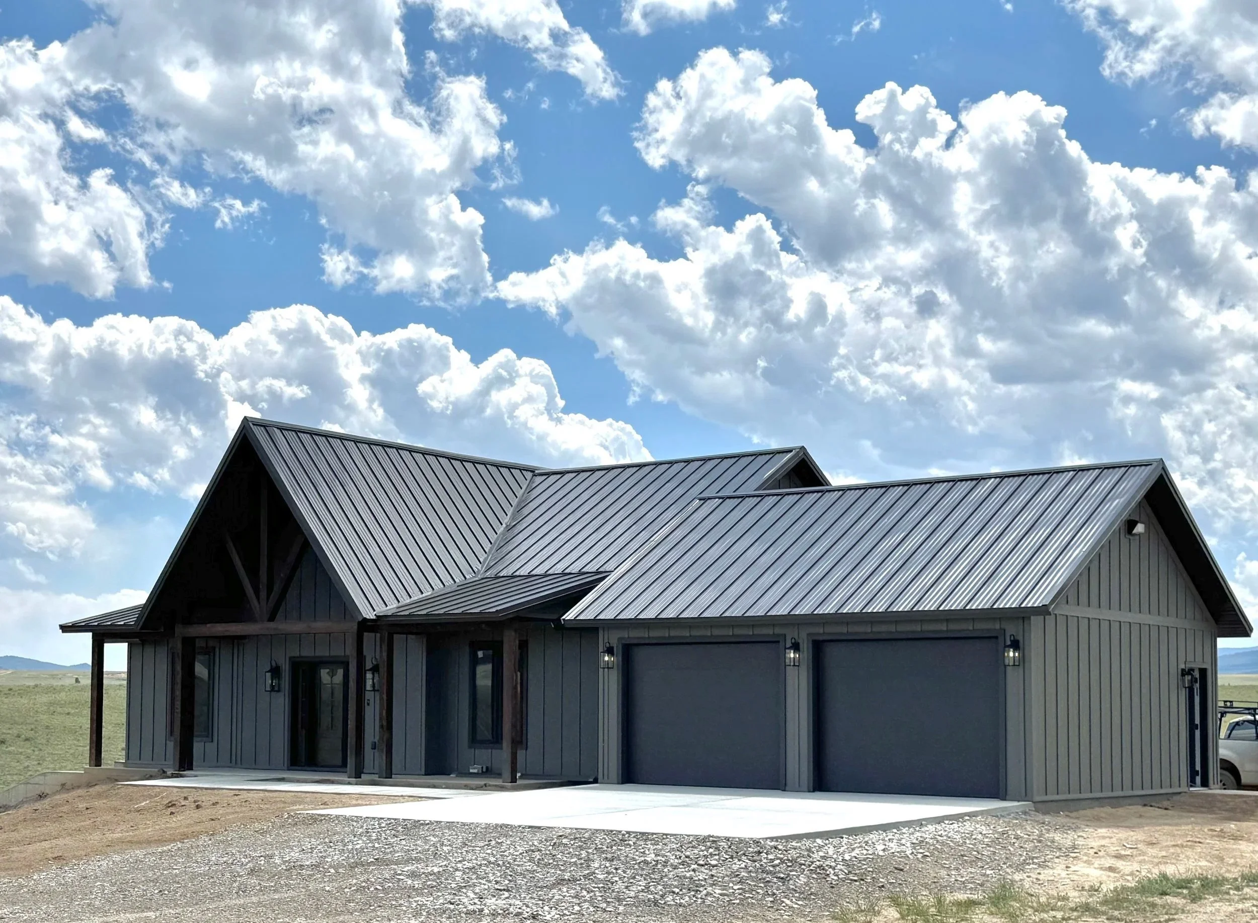Mihelich Custom Builders completed luxury custom home in Southwest Montana featuring black metal roofing, board and batten exterior, and dramatic vaulted roofline against a big sky backdrop.