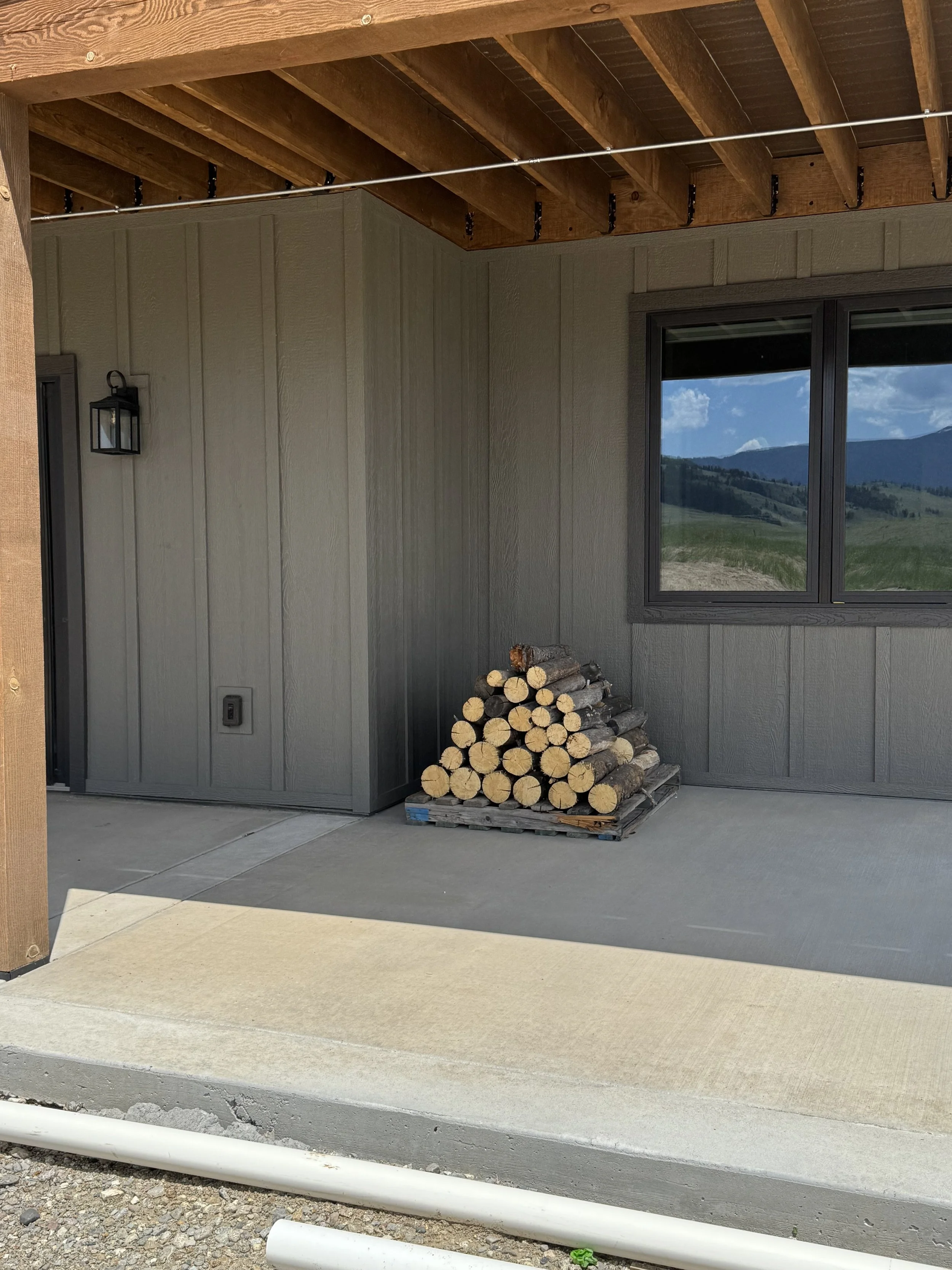 Custom covered porch with firewood storage — outdoor living detail by Mihelich Custom Builders, luxury home near Butte, Montana.