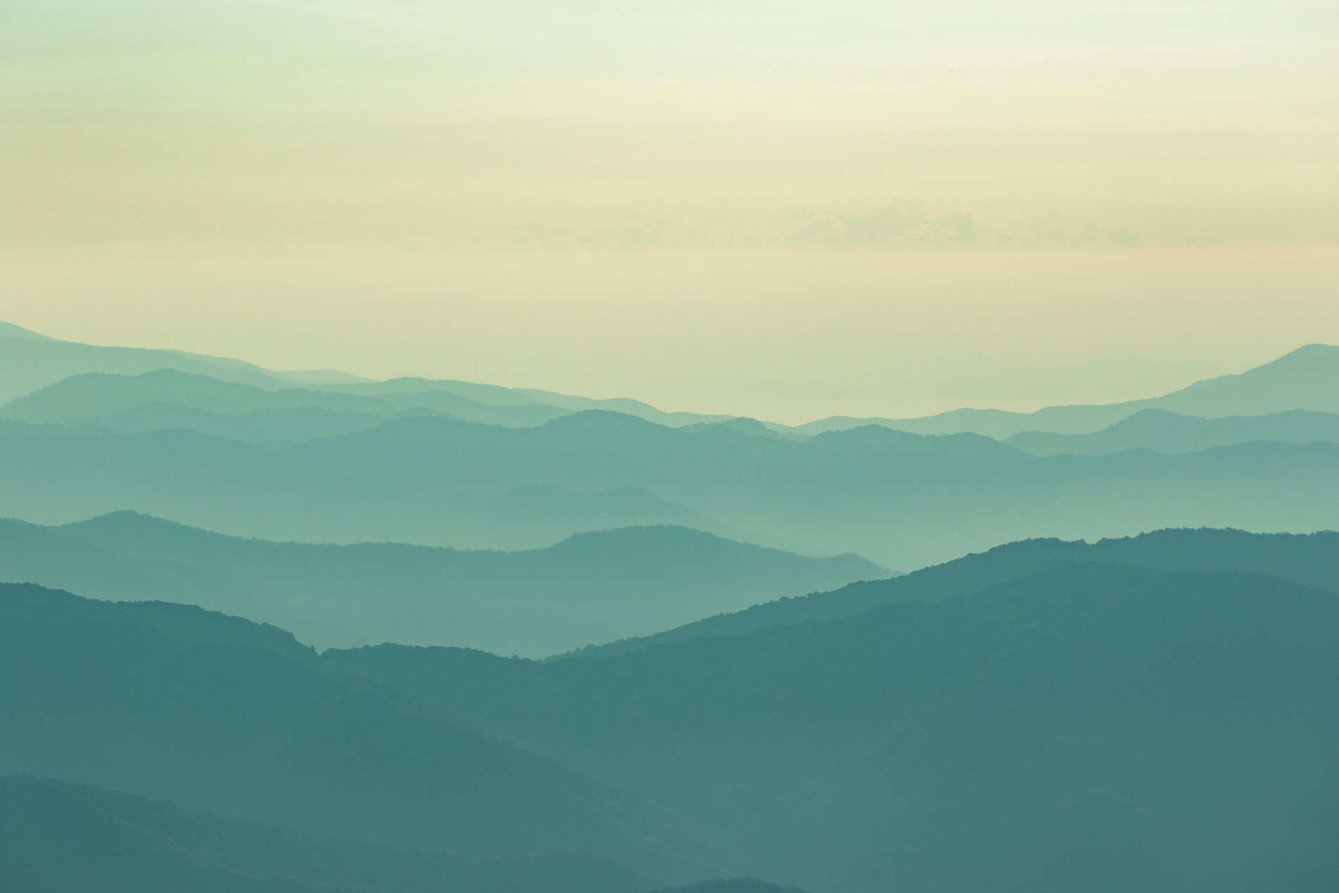 Multiple layers of blue-green mountains fading into the distance with a light, hazy sky above.
