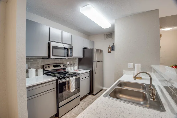 Kitchen with gray cabinets, stainless steel refrigerator and microwave, stove, gray countertops, and a double sink with a faucet.