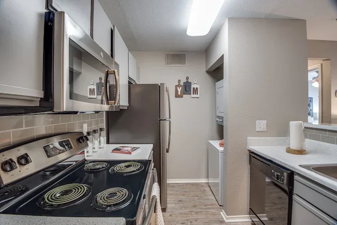 Kitchen with stove, microwave, refrigerator, and a laundry area with a washing machine and wall decor saying 'YUM'.