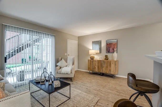 Living room with sliding glass door, armchair with throw blanket, wooden sideboard with lamps and art, and barstool with a curved back.