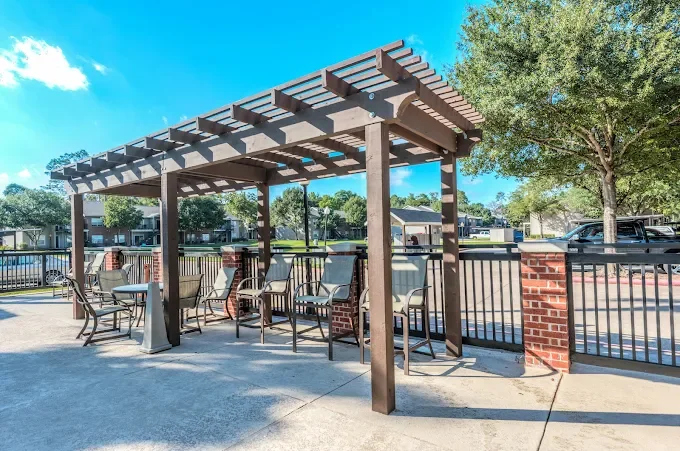 Outdoor seating area with wooden pergola and metal chairs near a fence in a residential neighborhood.