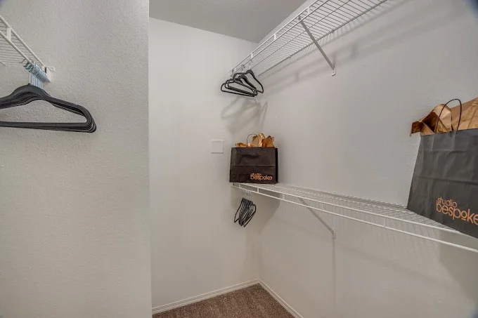 Empty walk-in closet with white wire shelves and a few black hangers, some shopping bags, and a black storage box.